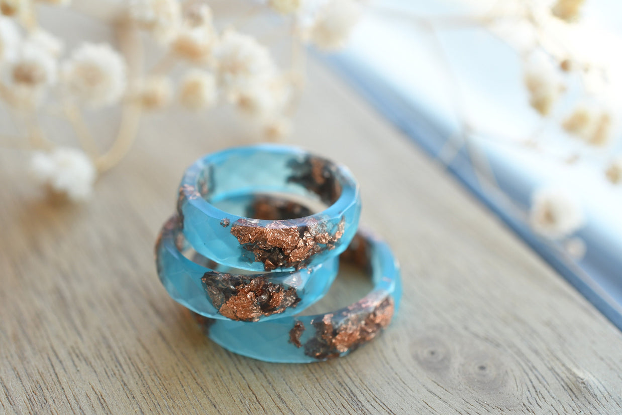 Blue spiral ring with brown accents on a wooden surface with blurred flowers in the background