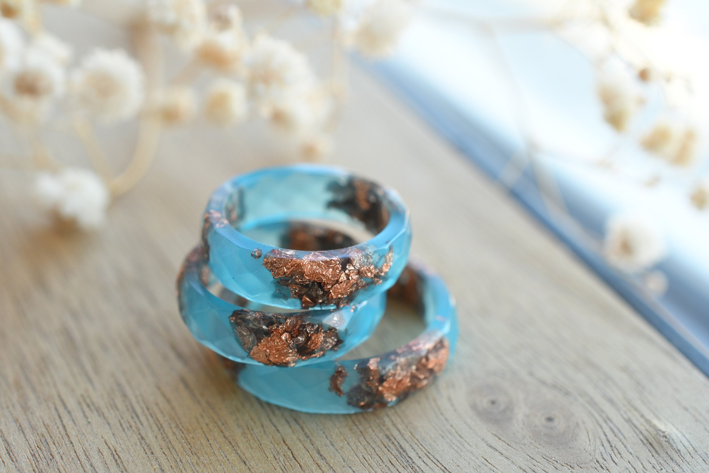 Blue spiral ring with brown accents on a wooden surface with blurred flowers in the background