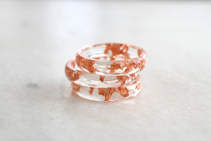 Stack of clear resin bracelets with red speckles on a light marble surface