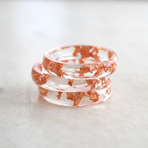 Stack of clear resin bracelets with red speckles on a light marble surface