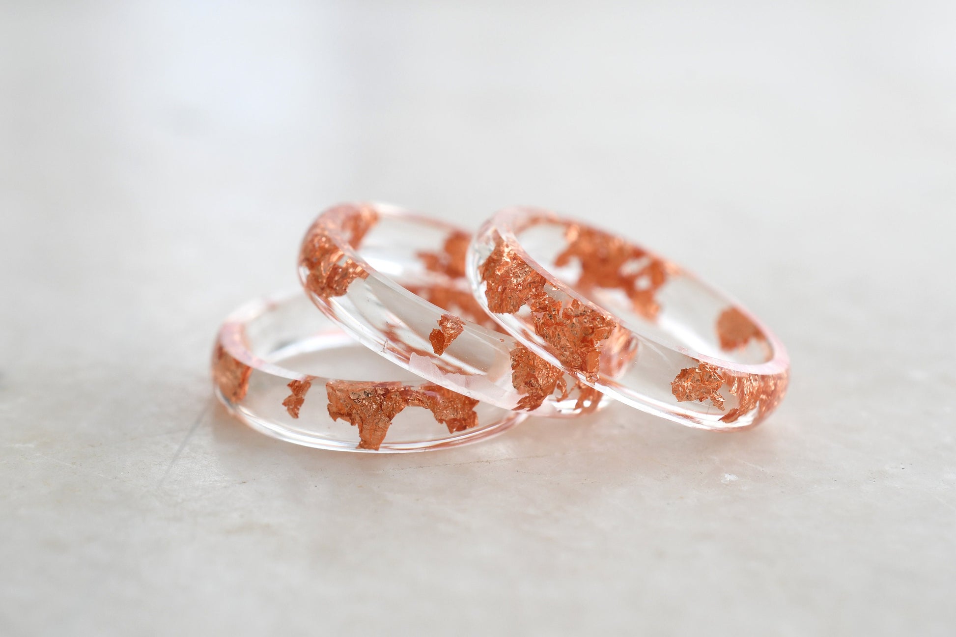 Two rose gold and clear resin rings on a light gray background