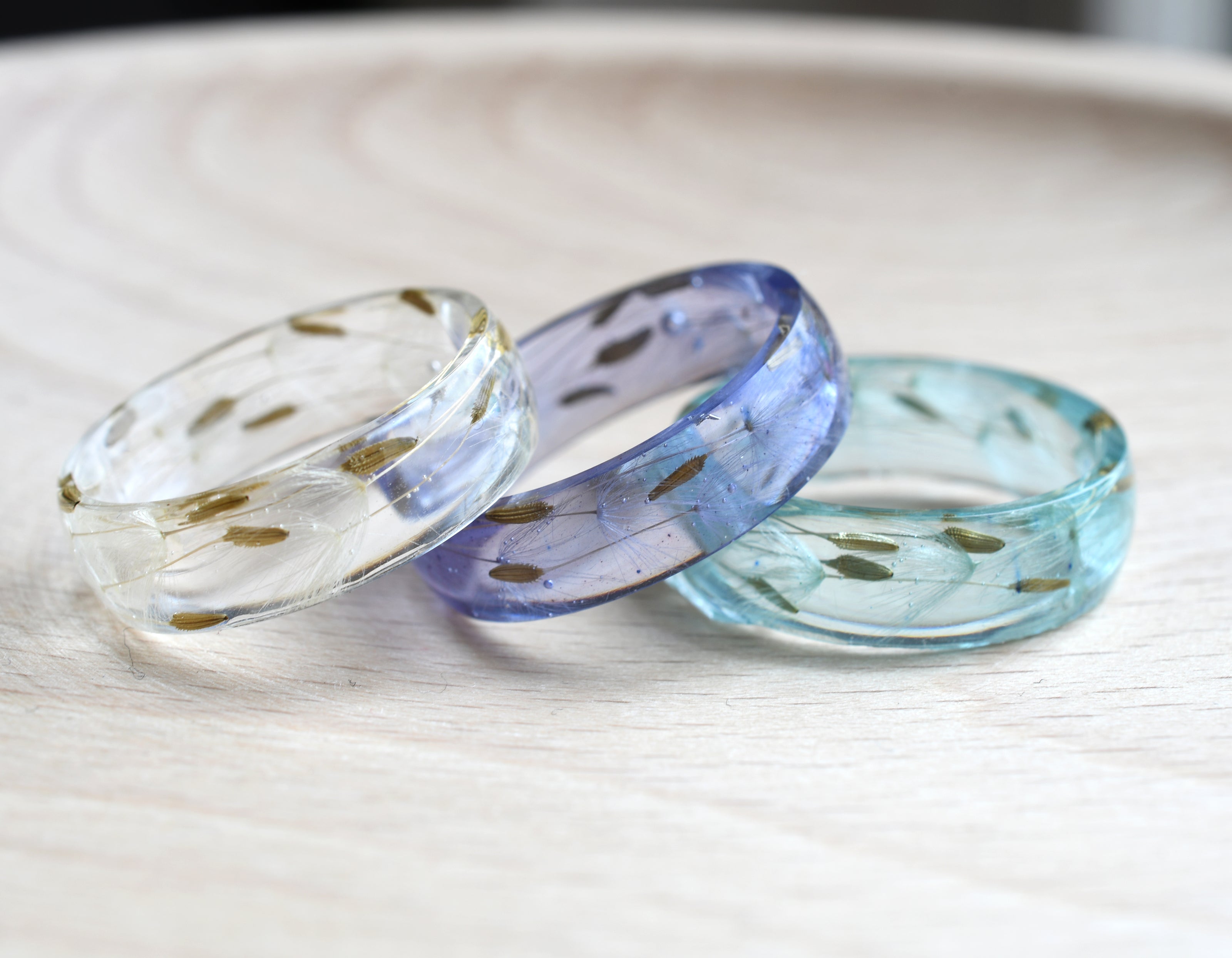 Two resin rings on a wooden surface, one with a clear finish and the other with a light blue and white color gradient.