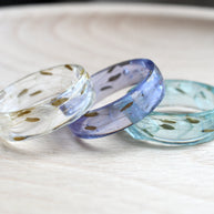 Two resin rings on a wooden surface, one with a clear finish and the other with a light blue and white color gradient.