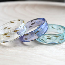 Two resin rings on a wooden surface, one with a clear finish and the other with a light blue and white color gradient.