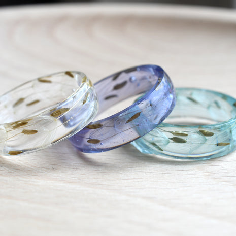 Two resin rings on a wooden surface, one with a clear finish and the other with a light blue and white color gradient.
