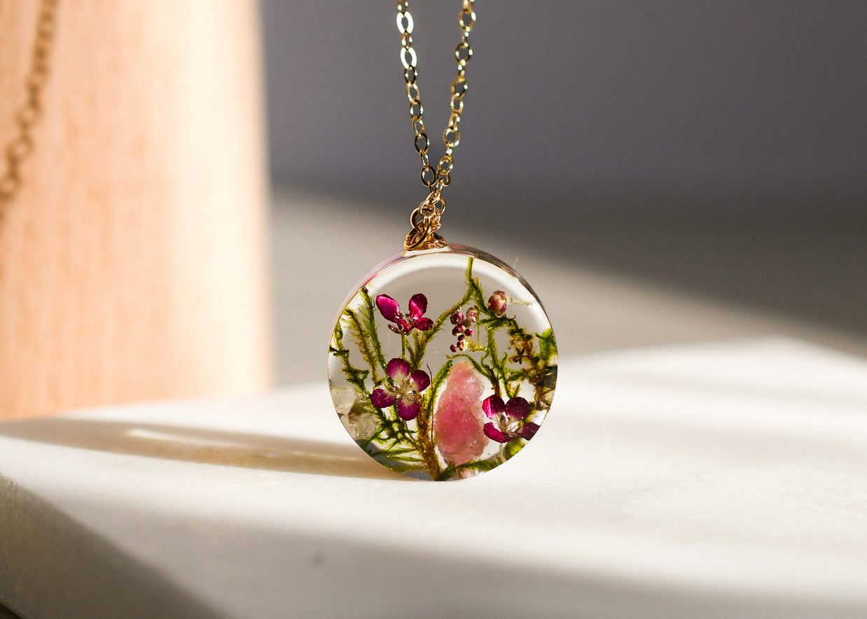 Close-up of moss, alyssum, and tourmaline crystal preserved inside clear resin pendant