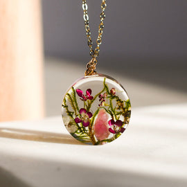 Close-up of moss, alyssum, and tourmaline crystal preserved inside clear resin pendant