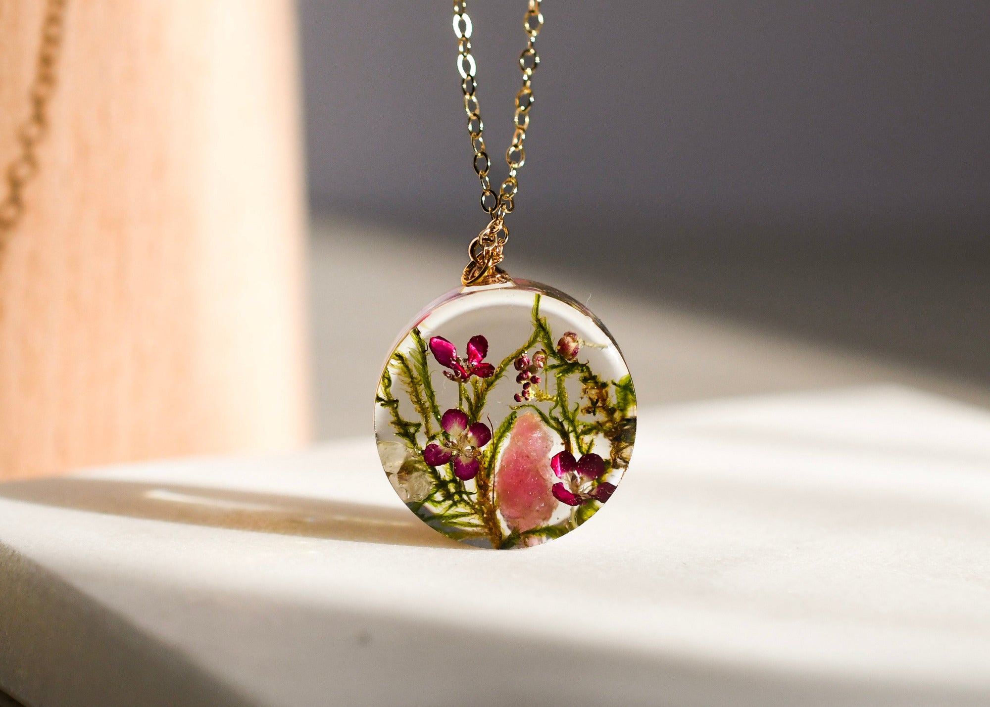 Close-up of moss, alyssum, and tourmaline crystal preserved inside clear resin pendant