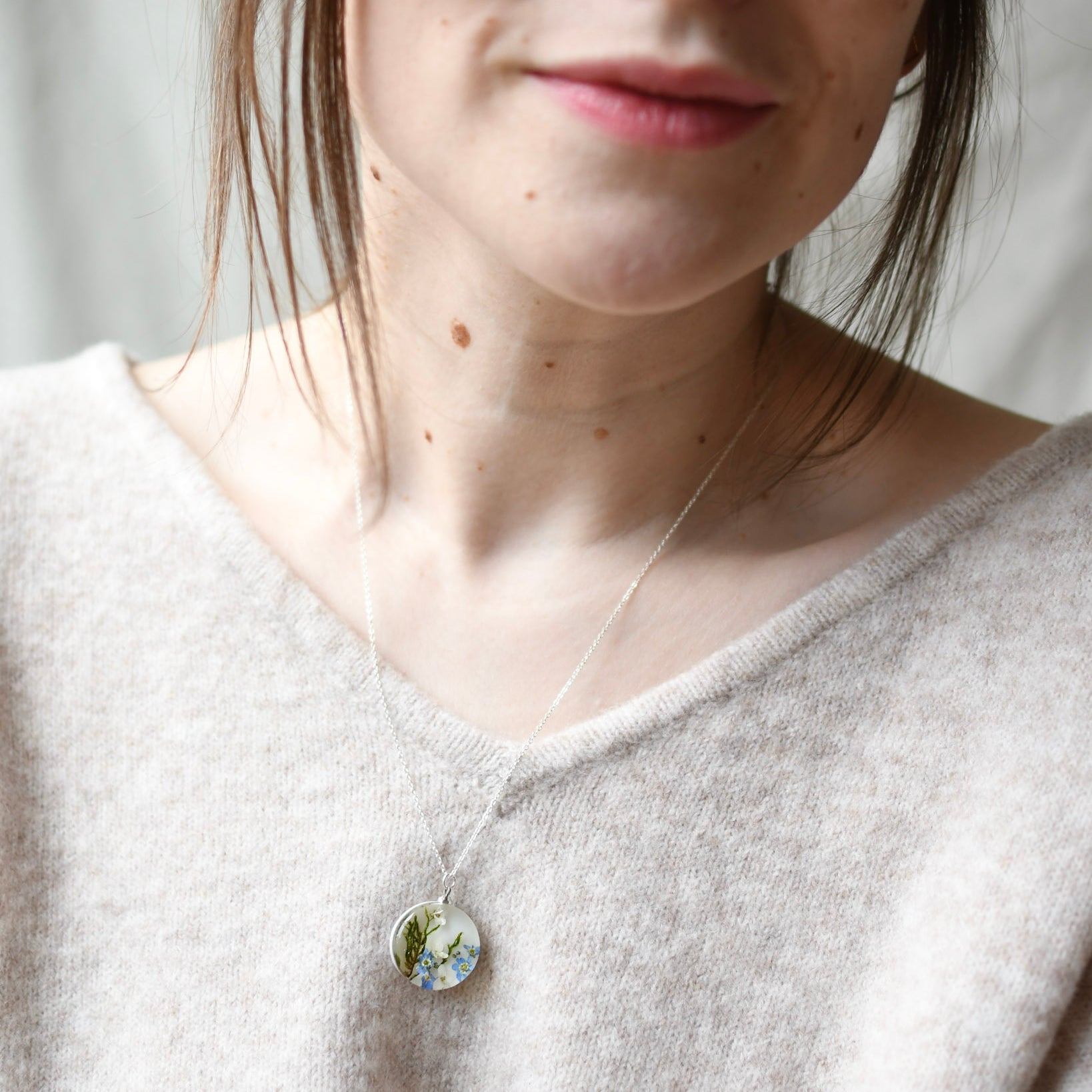 Person wearing a necklace with a round pendant, set against a neutral background