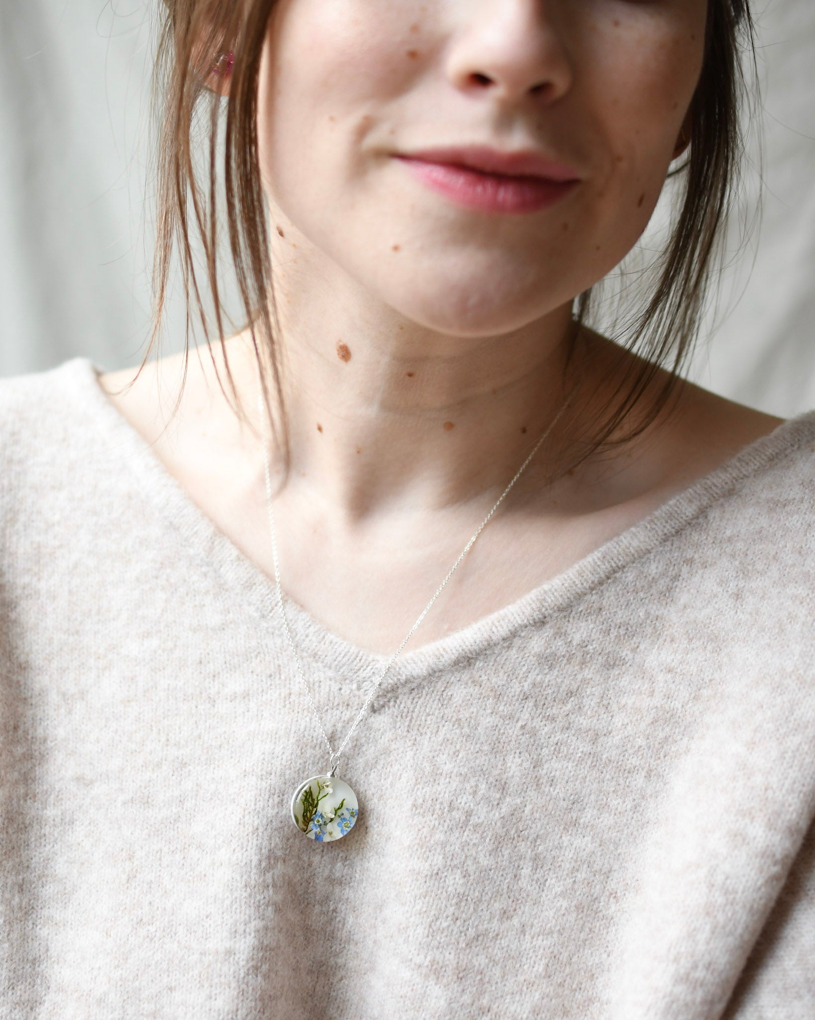 Person wearing a necklace with a round pendant, set against a neutral background
