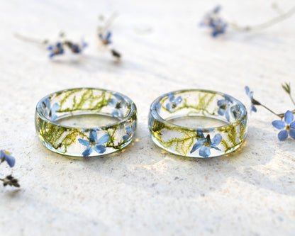 Two transparent rings with embedded flowers on a light surface.