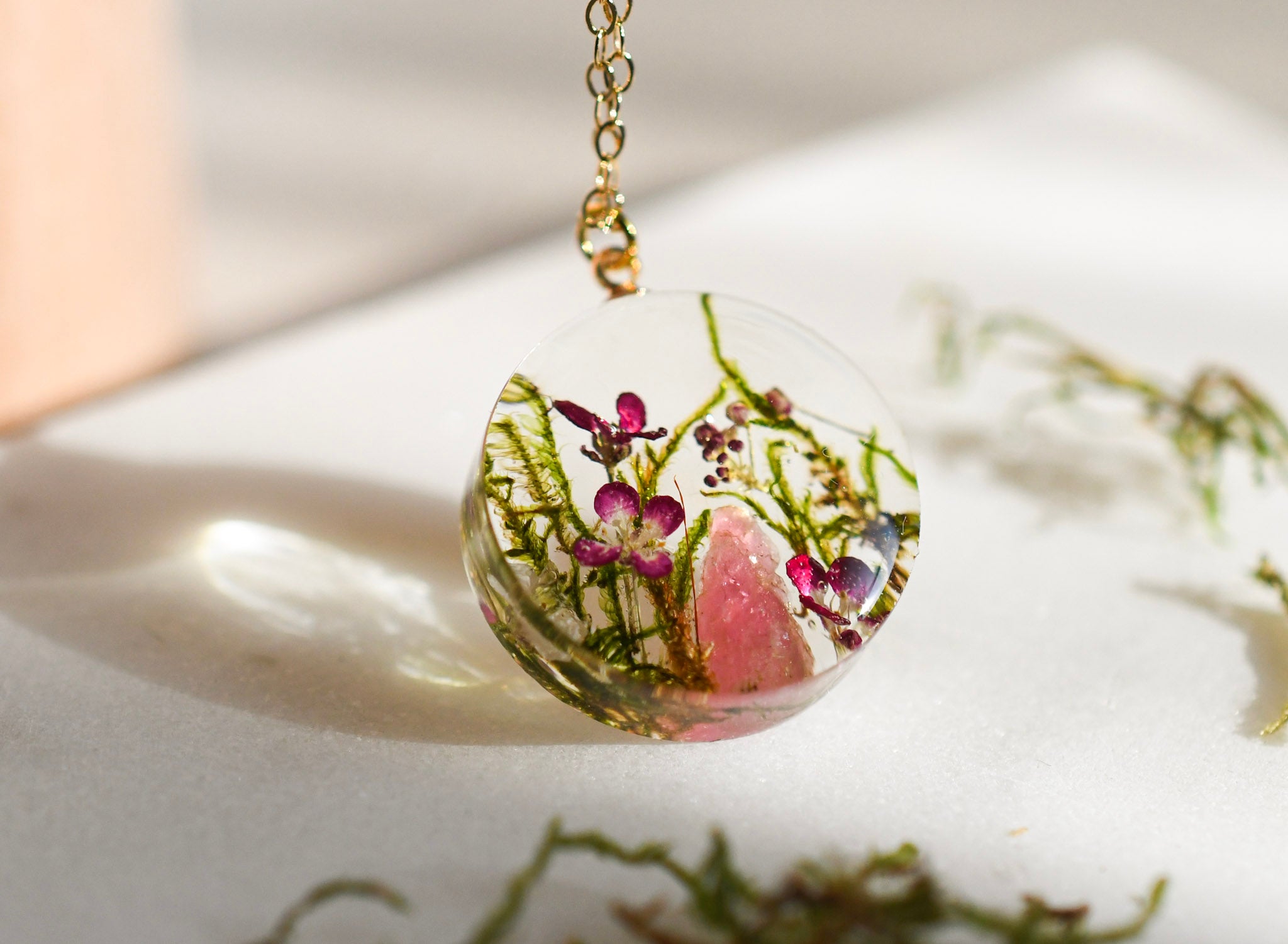 Necklace with a clear pendant featuring pink and green natural elements on a light background