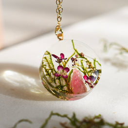 Necklace with a clear pendant featuring pink and green natural elements on a light background