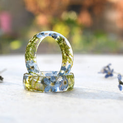 Two clear resin rings with embedded flowers on a light surface with blurred natural background