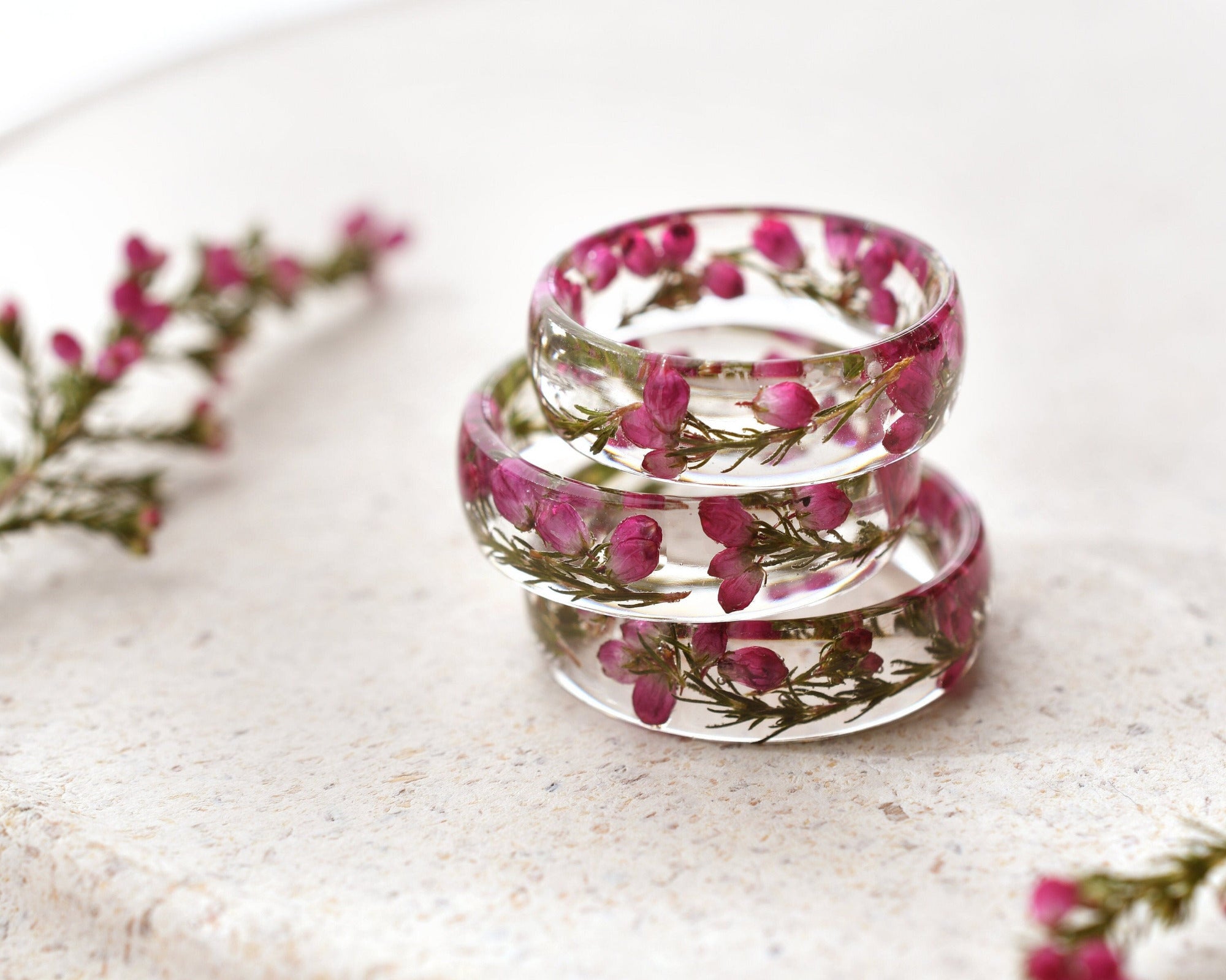 Stack of clear resin rings with pink heather flowers on a light surface
