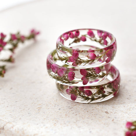 Stack of clear resin rings with pink heather flowers on a light surface