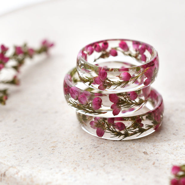 Stack of clear resin rings with pink heather flowers on a light surface