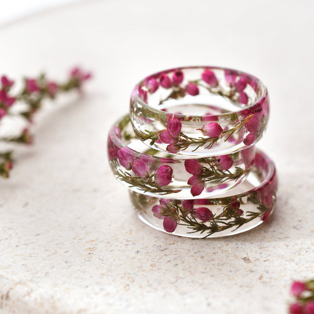 Stack of clear resin rings with pink heather flowers on a light surface
