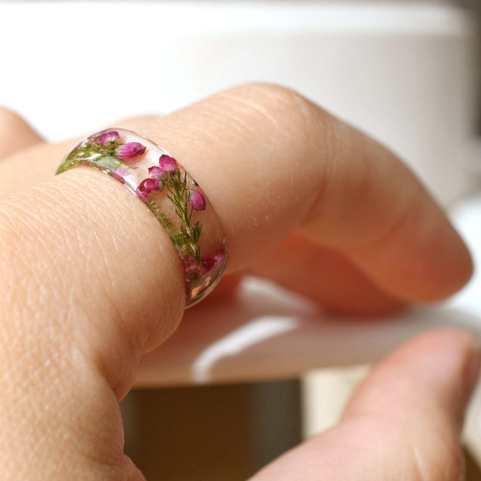 Hand model wearing pink heather resin ring, showcasing natural floral detail