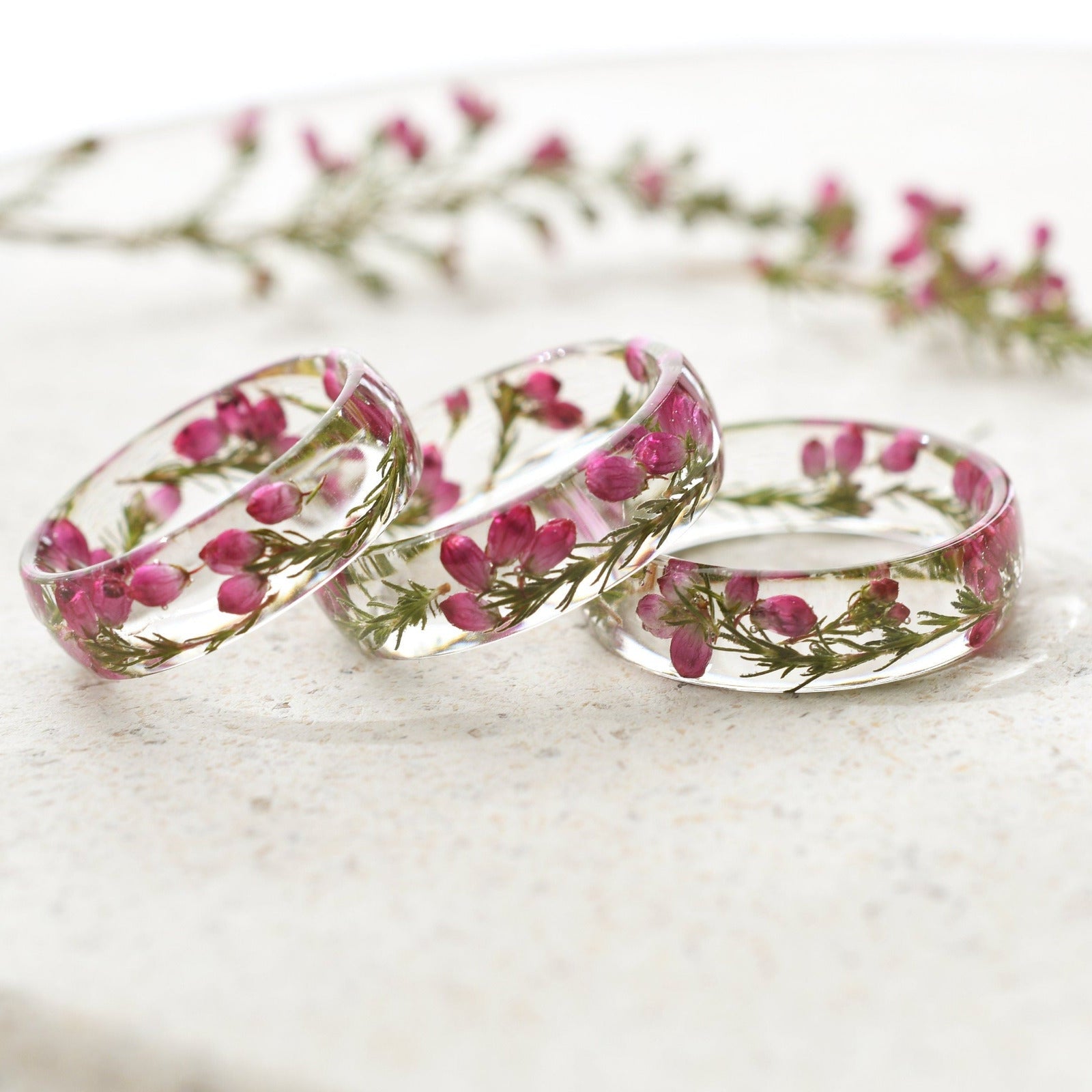 Three transparent rings with pink flowers on a white marble surface
