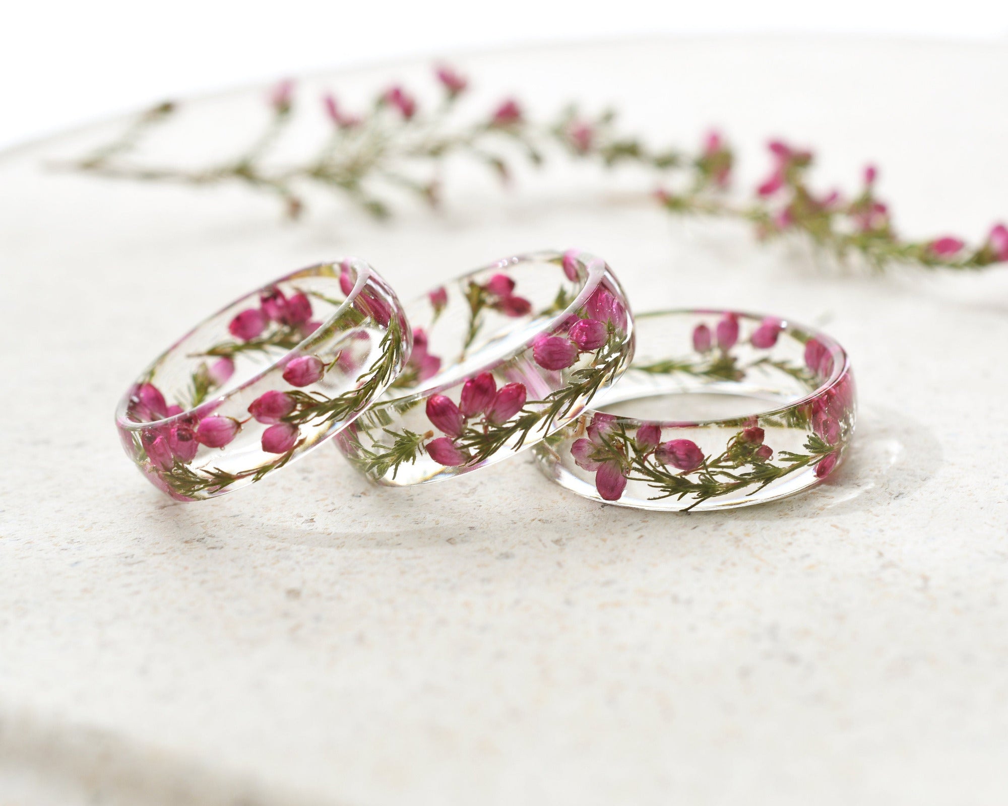 Three transparent rings with pink flowers on a white marble surface