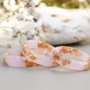 Three pink and gold rings on a light surface with blurred natural background