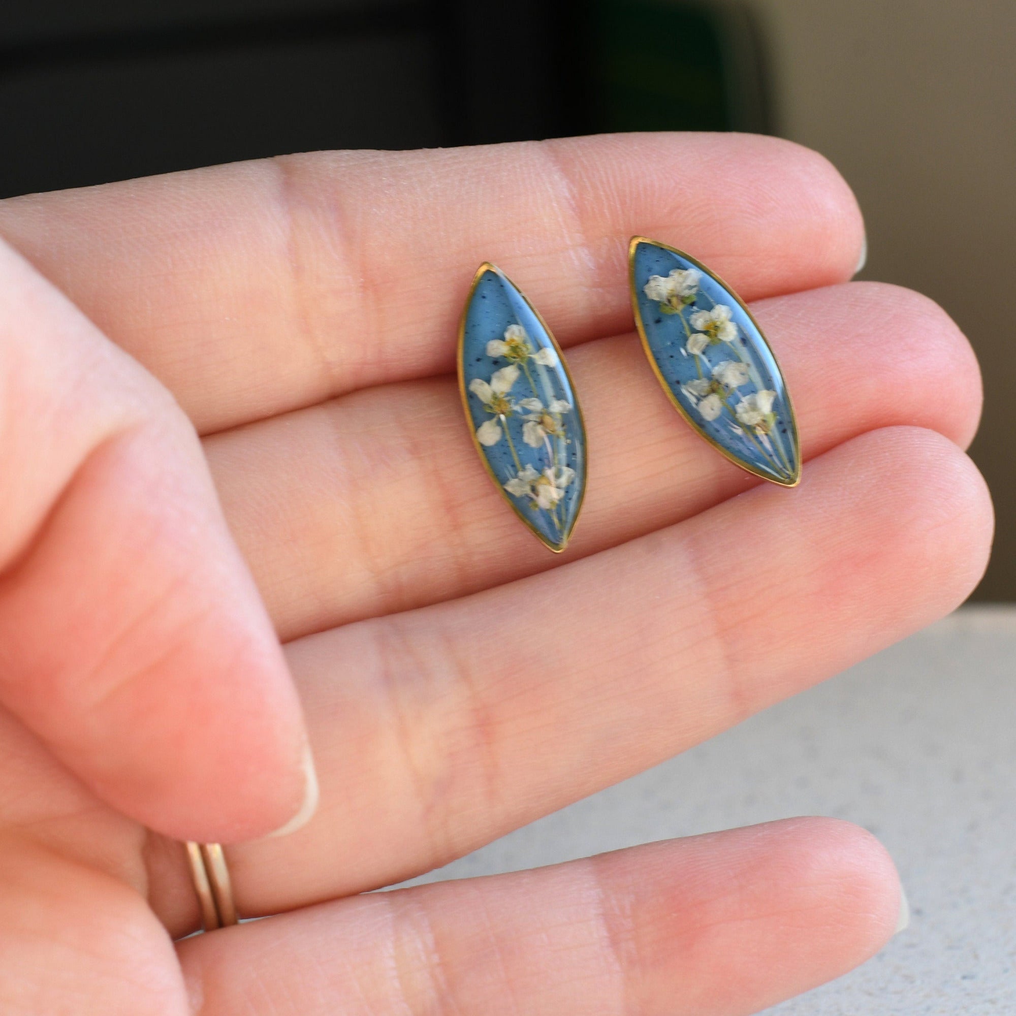 Blue earrings with floral design held in a hand