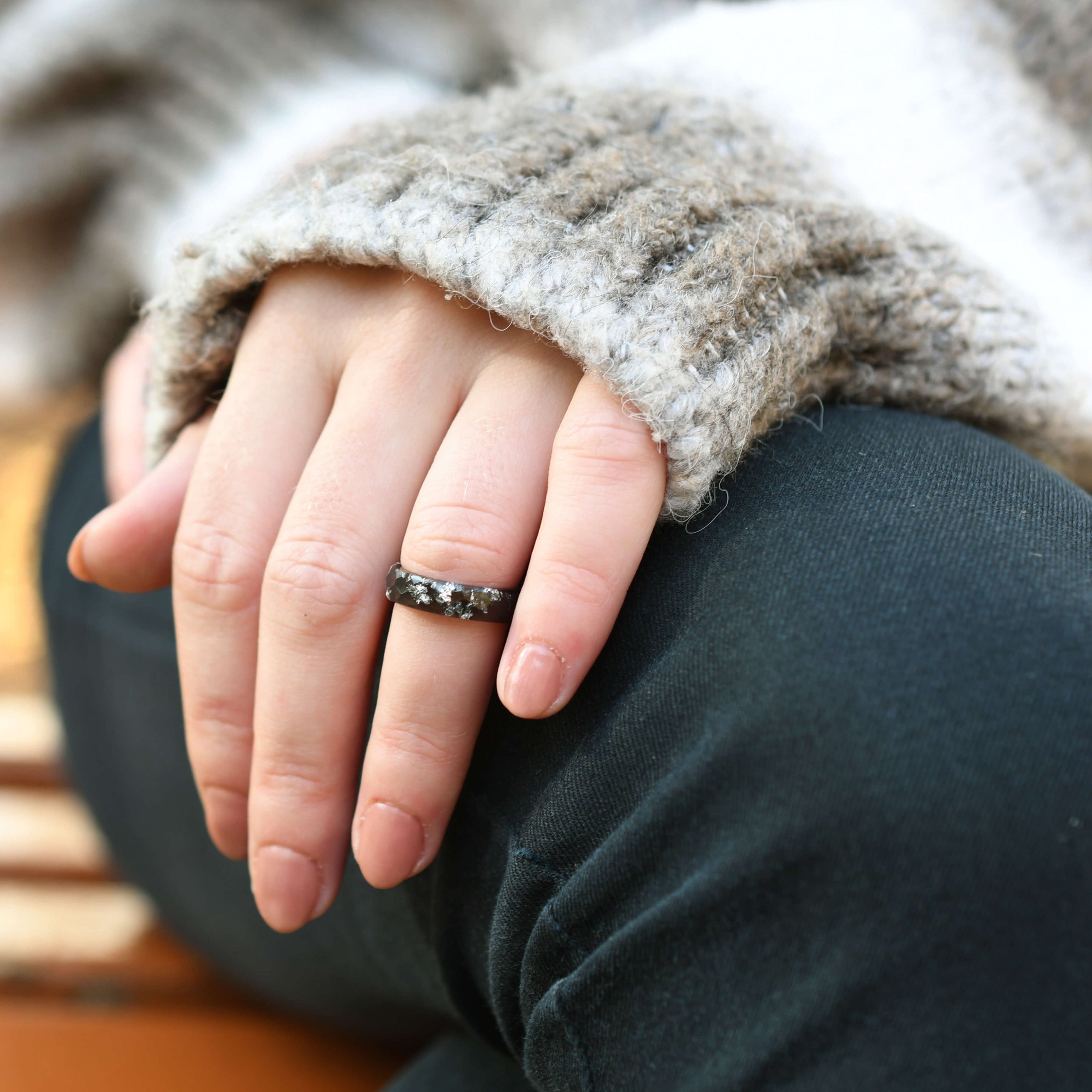 Close-up of a hand wearing a ring with a textured sleeve and dark pants.
