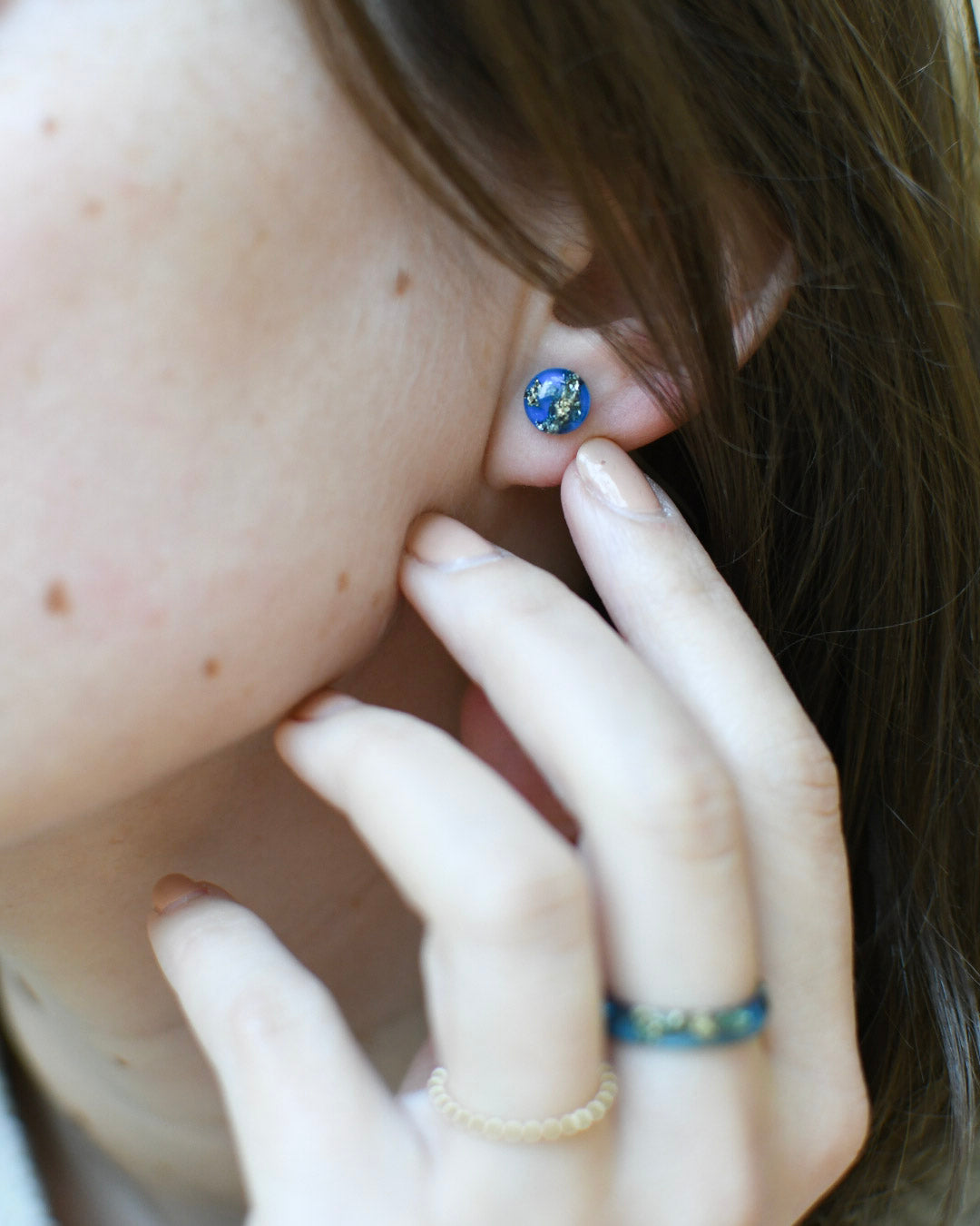 Blue and gold resin stud earrings worn on ear — hypoallergenic handmade jewelry