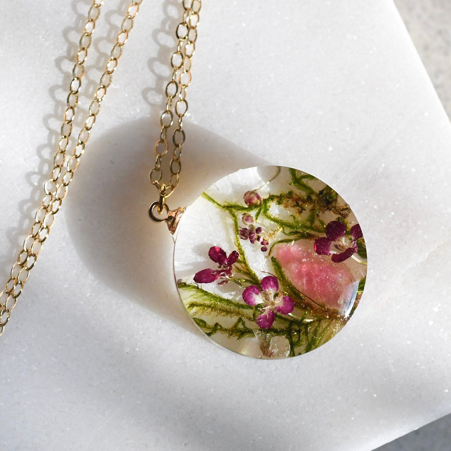 Necklace with a round pendant featuring pressed flowers on a white background
