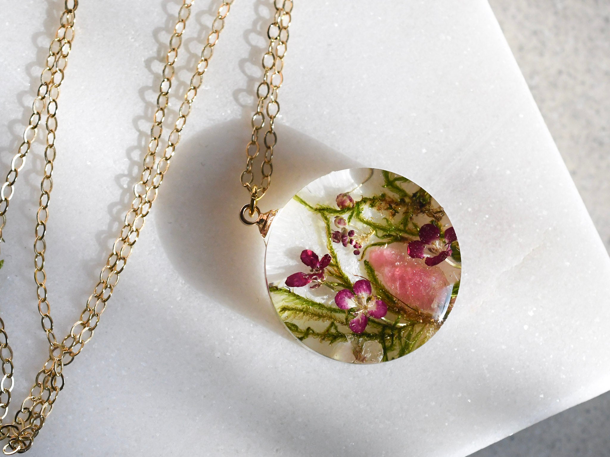 Necklace with a round pendant featuring pressed flowers on a white background