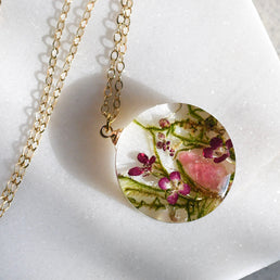 Necklace with a round pendant featuring pressed flowers on a white background