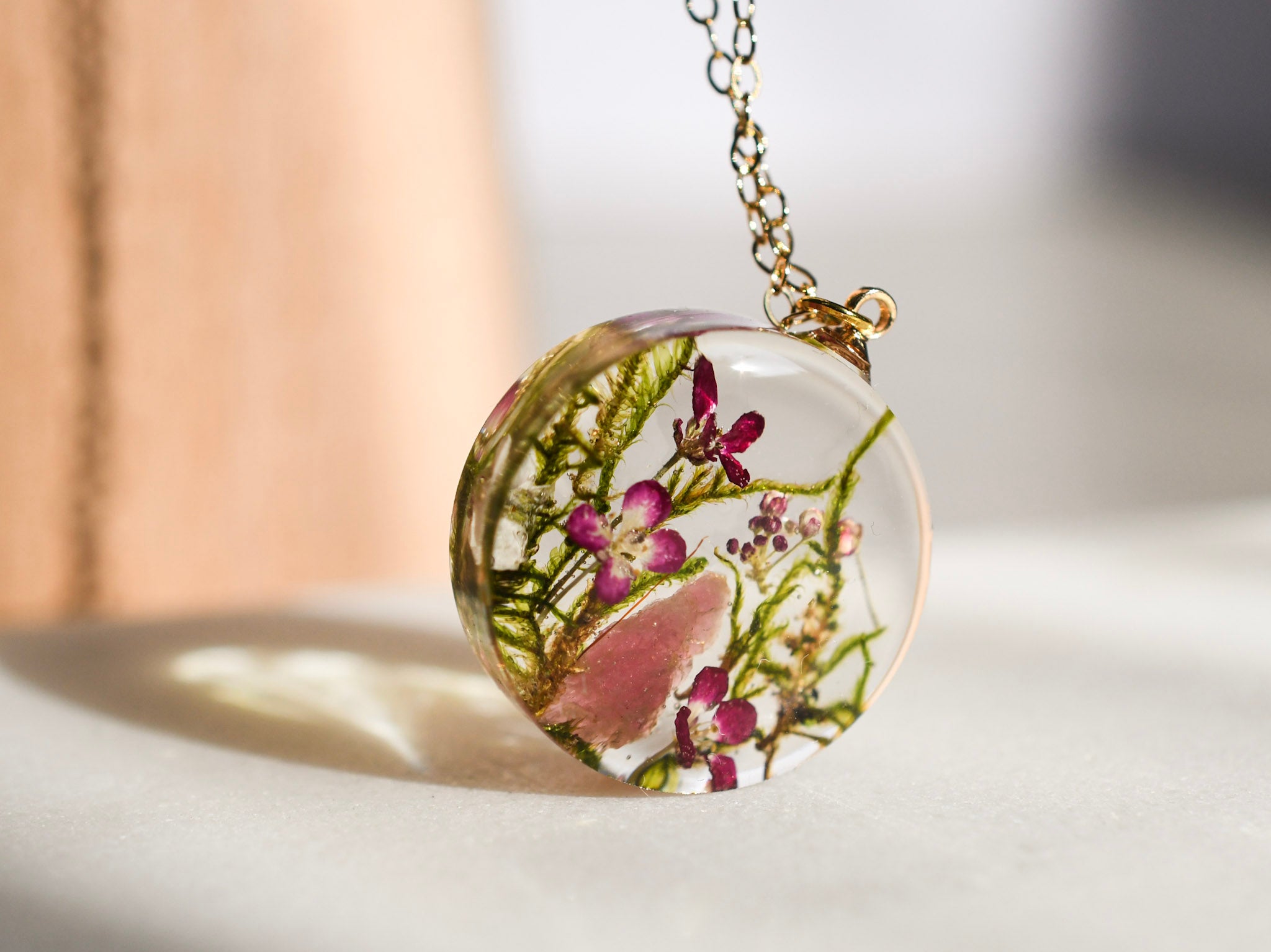 Moss and pink crystal resin necklace in sunlight