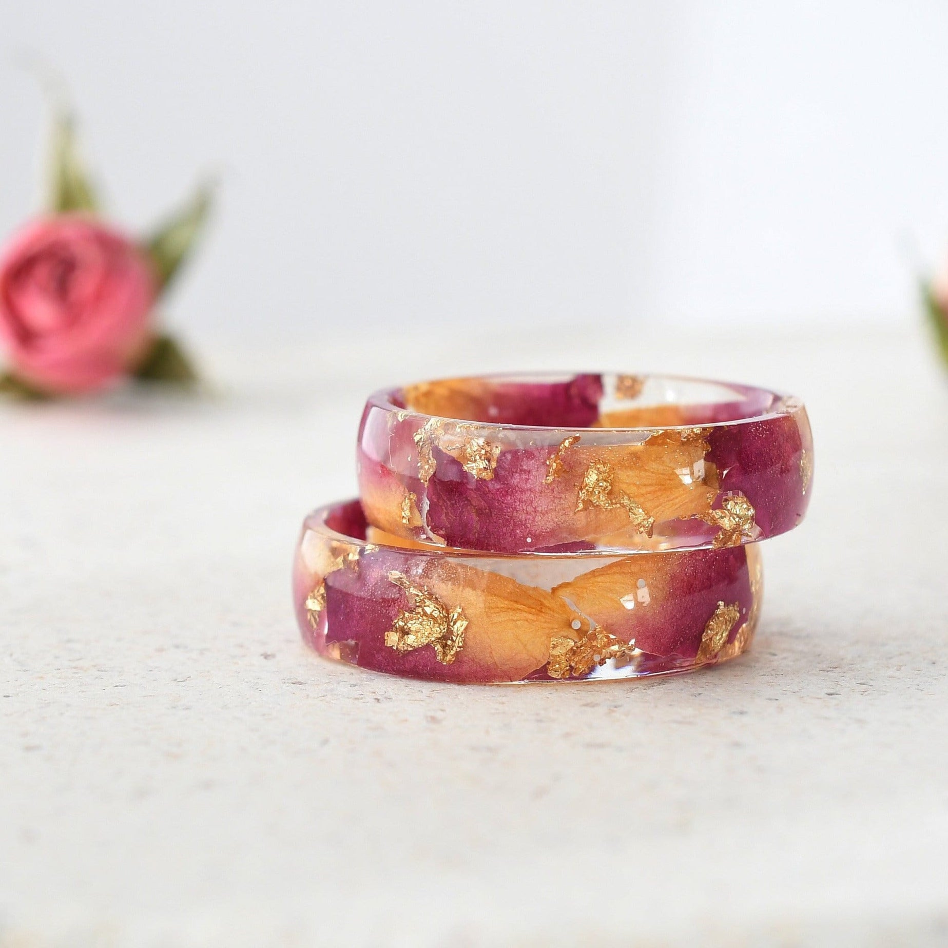 Resin ring with rose petals and gold leaf shown flat on soft background