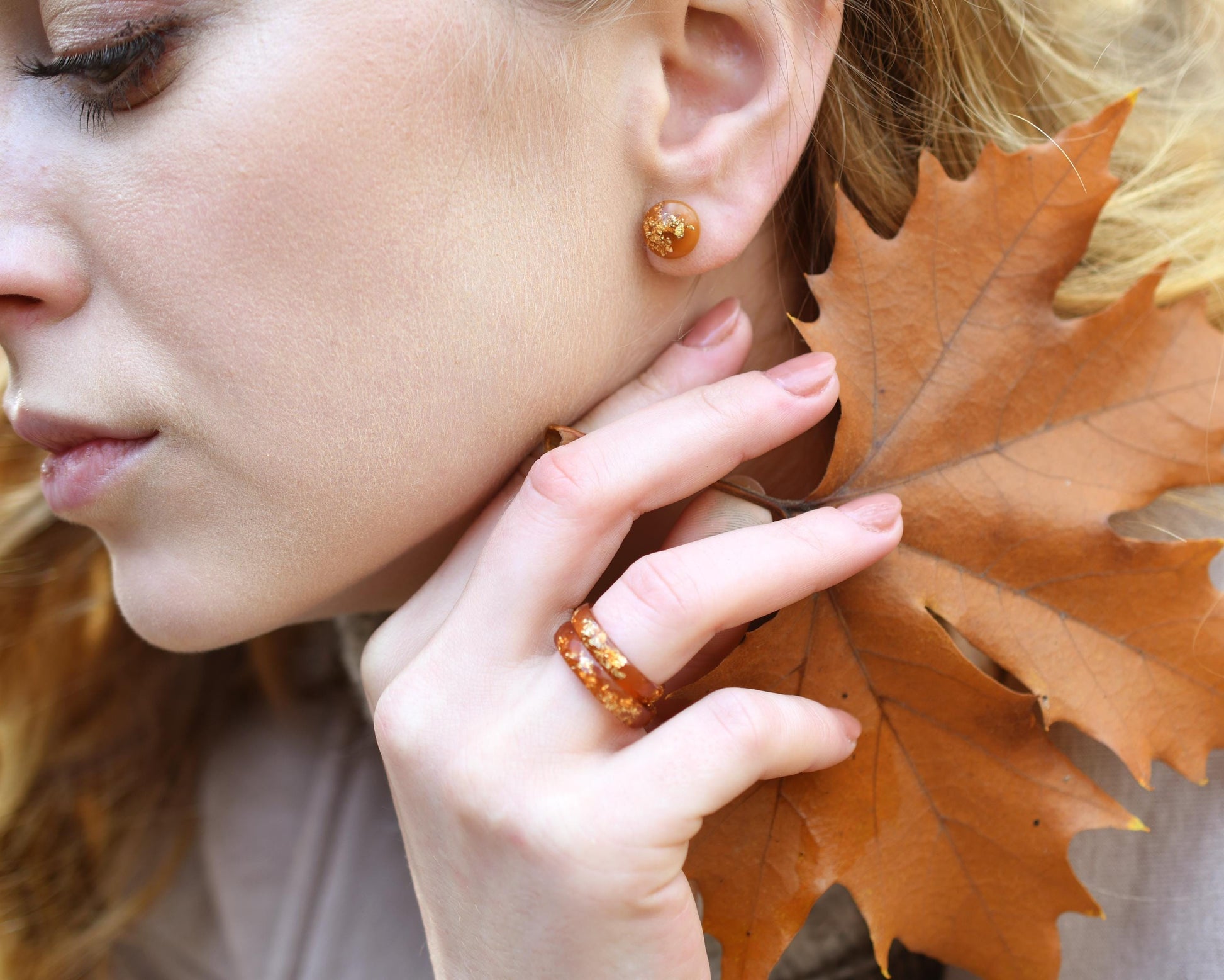 Woman wearing amber earrings with a close-up of her face and hand holding an autumn leaf.
