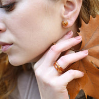 Woman wearing amber earrings with a close-up of her face and hand holding an autumn leaf.