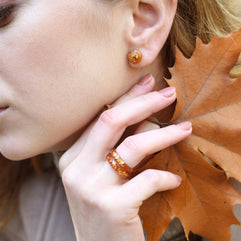 Woman wearing amber earrings with a close-up of her face and hand holding an autumn leaf.
