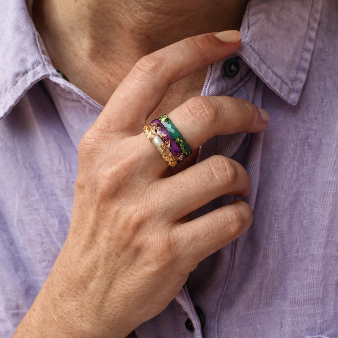 Close-up of a hand wearing a colorful ring on a light purple shirt.