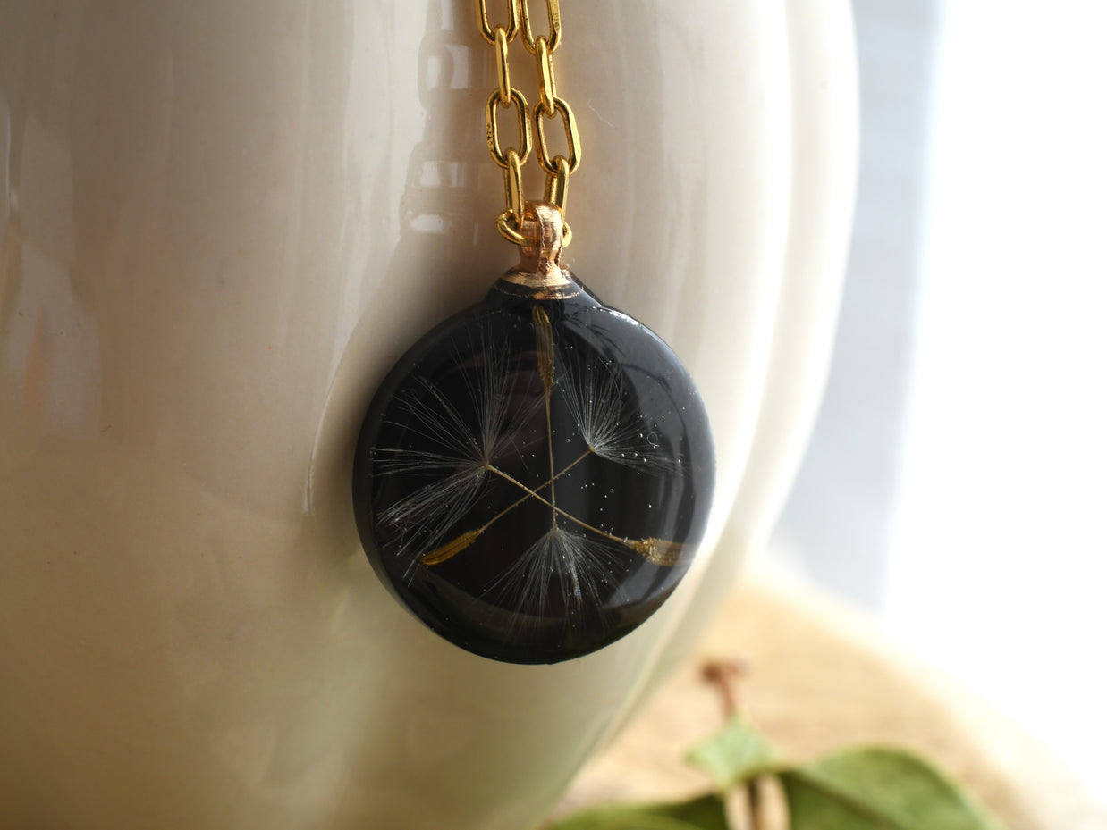 Nature-inspired necklace with real dandelion seed preserved in black resin, gold chain detail