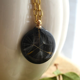 Nature-inspired necklace with real dandelion seed preserved in black resin, gold chain detail
