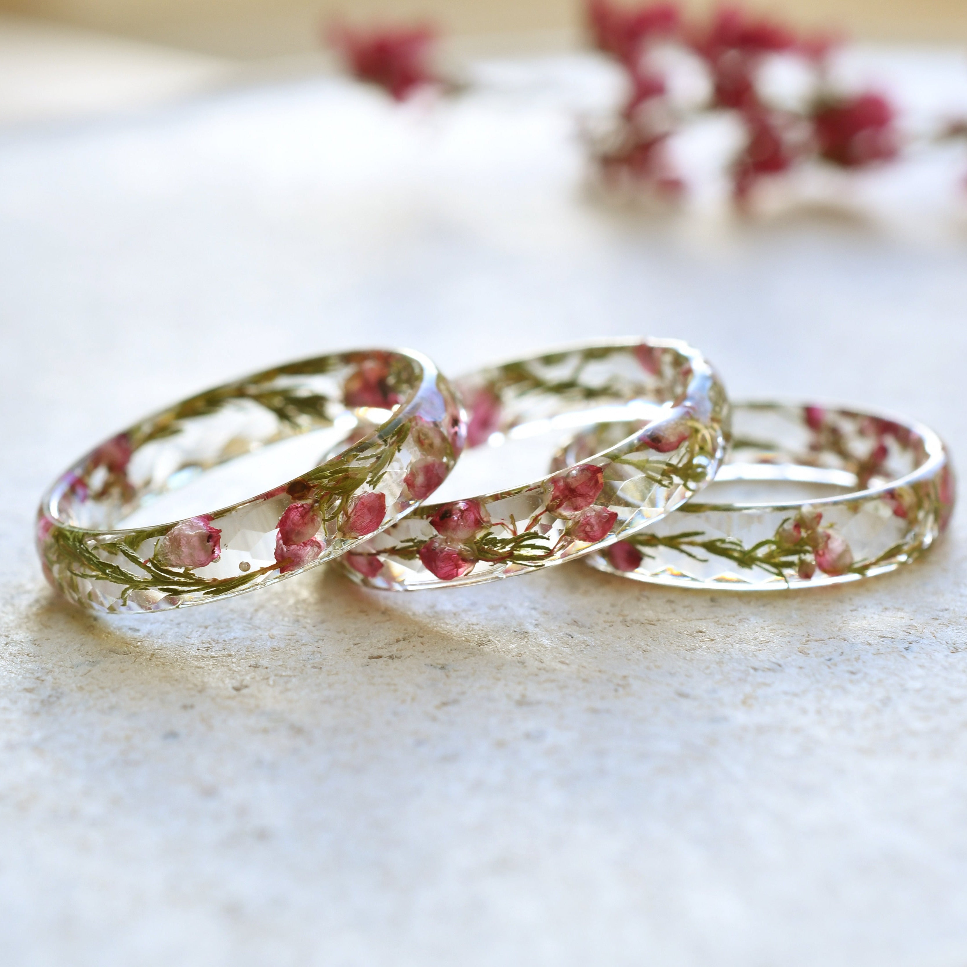 Three floral-patterned clear rings on a light surface with blurred flowers in the background