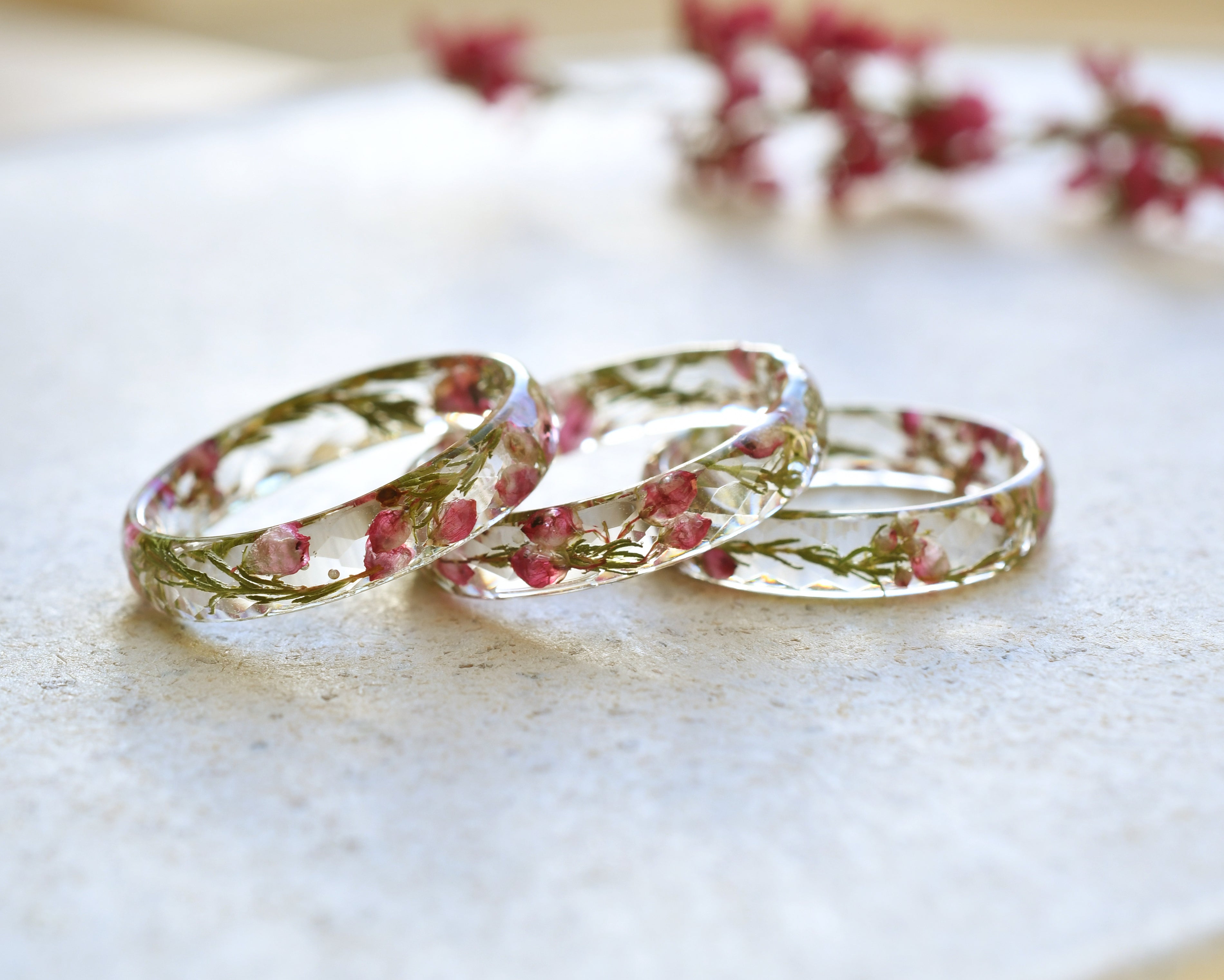 Three floral-patterned clear rings on a light surface with blurred flowers in the background