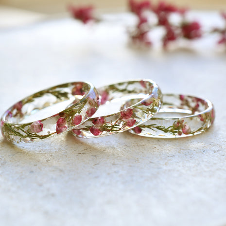 Three floral-patterned clear rings on a light surface with blurred flowers in the background