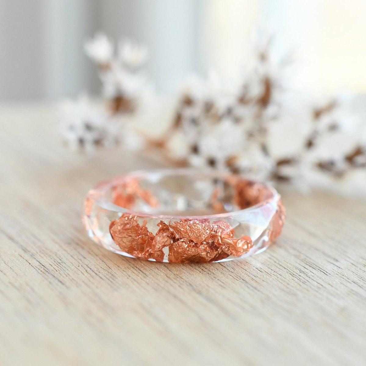 Transparent resin ring with copper flakes on wooden background