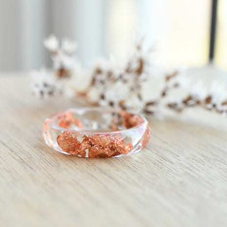 Transparent resin ring with copper flakes on wooden background